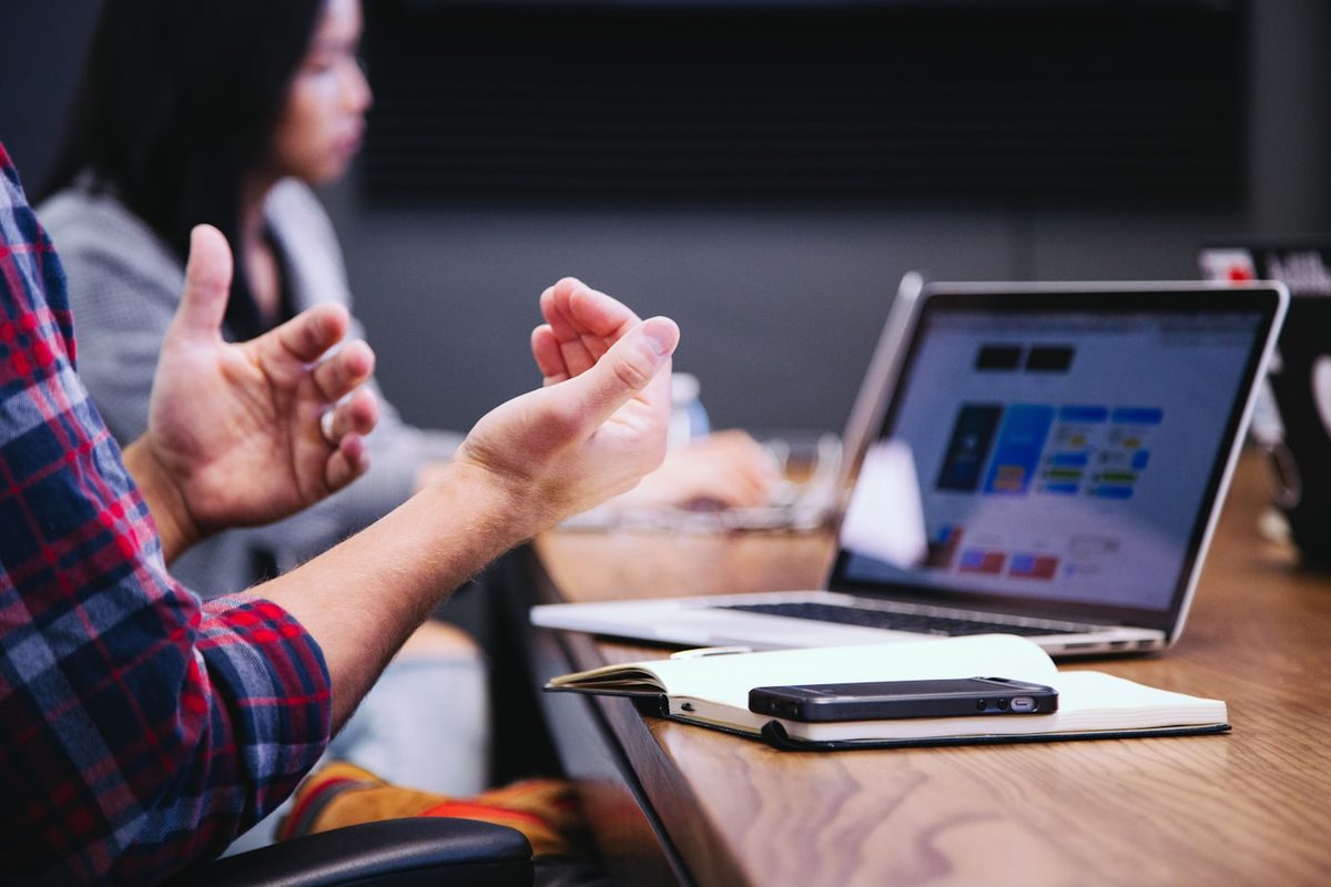 Hands gesturing mid-conversation across a table with an open laptop