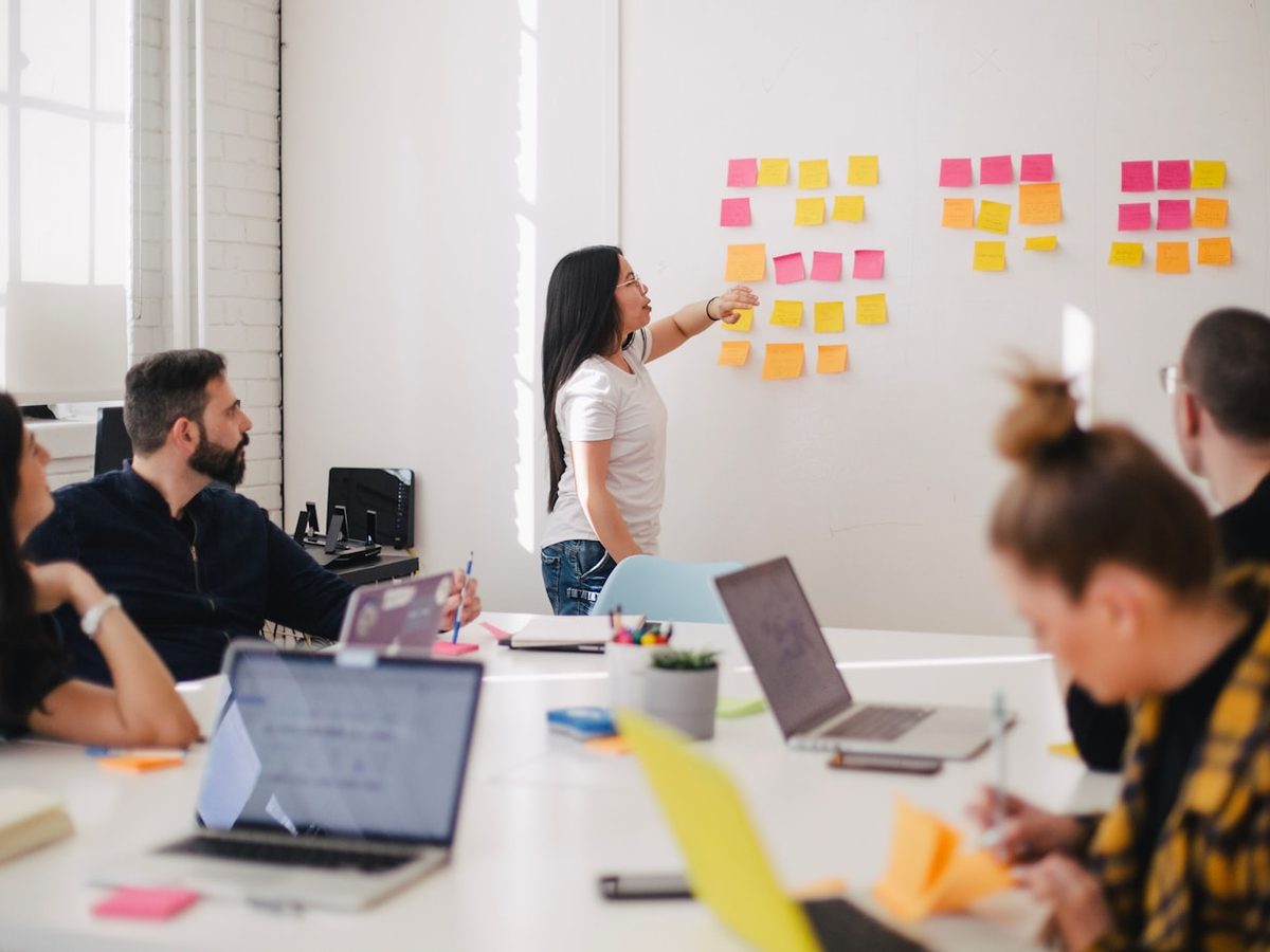 A founder mapping out ideas on a wall of sticky notes while a team works around a table
